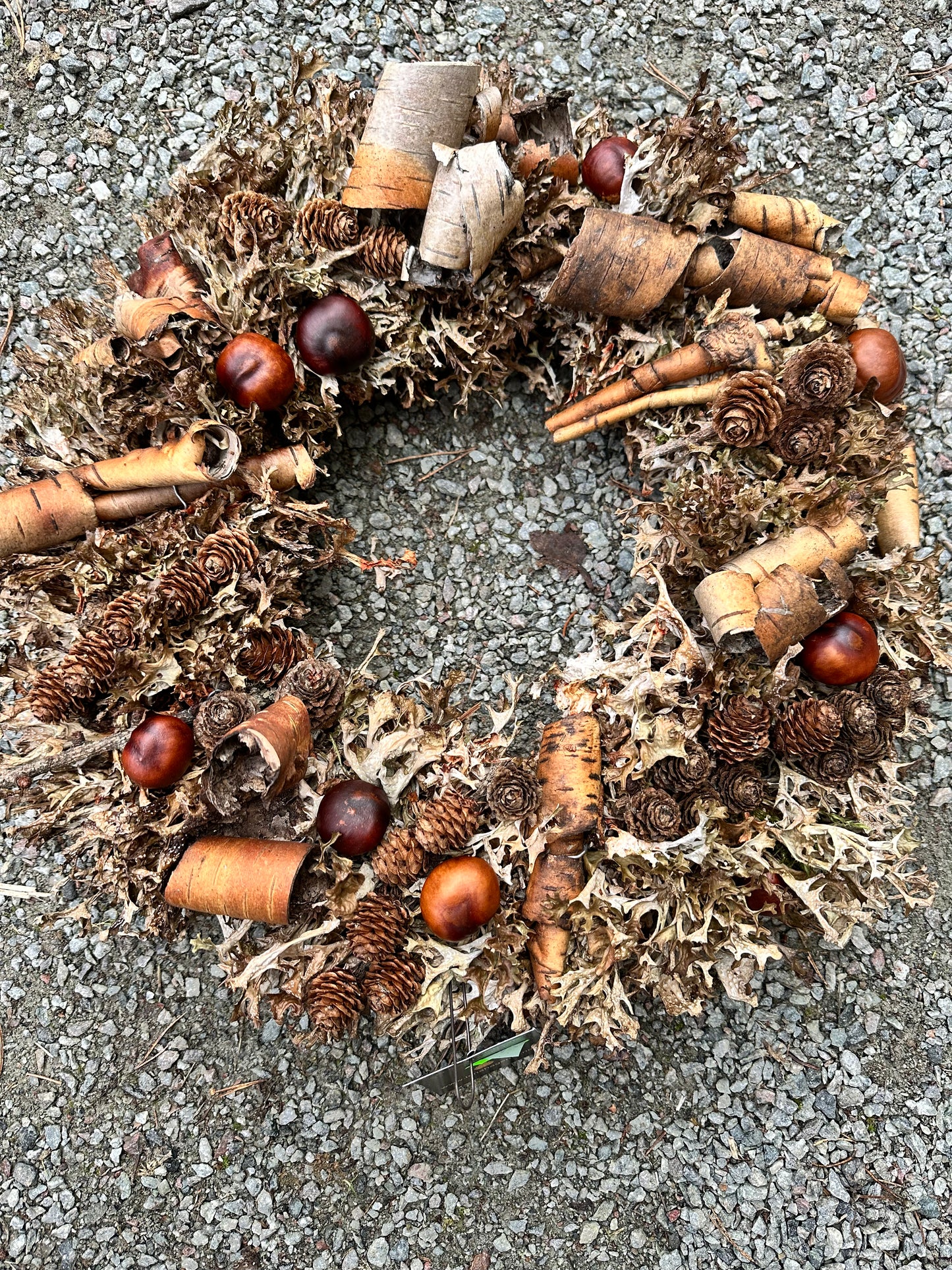 Norsk natur med never, hestekastanje og brødlav møter lerk i denne håndlagde kransen. Basen er av halmkrans
